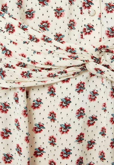 Tessuto color crema con motivo floreale rosso e blu, piccoli puntini neri, dettaglio di tessuto arricciato e annodato, e bottone rivestito.