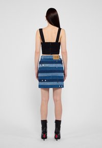 Svart samlad crop top med breda axelband, kombinerad med en blå denim minikjol med horisontella ränder och silverdetaljer.