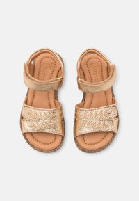 Złote metaliczne sandały z dwiema szerokimi paskami, teksturowanymi detalami i wyściełaną wkładką w kolorze brązowym. Elastyczna gumowa podeszwa dla komfortu i przyczepności.