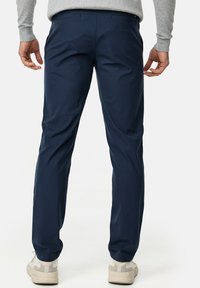 Navy blue trousers with a smooth texture, tailored fit, and subtle back pockets. Worn with light-colored sneakers.