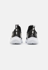 Black and white athletic shoes with a textured upper, pull tabs, and a white sole featuring a tread pattern. Logo accents on the heel.