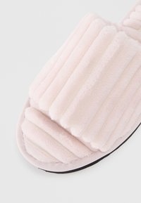 Zapatilla de slide de felpa rosa con textura estriada, parte superior de tela suave y suela de goma negra. Presenta una tira ancha y diseño de punta redondeada.