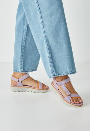 Purple and orange sandals with textured straps, a cushioned white sole, and an open-toe design, worn with light blue wide-leg jeans.