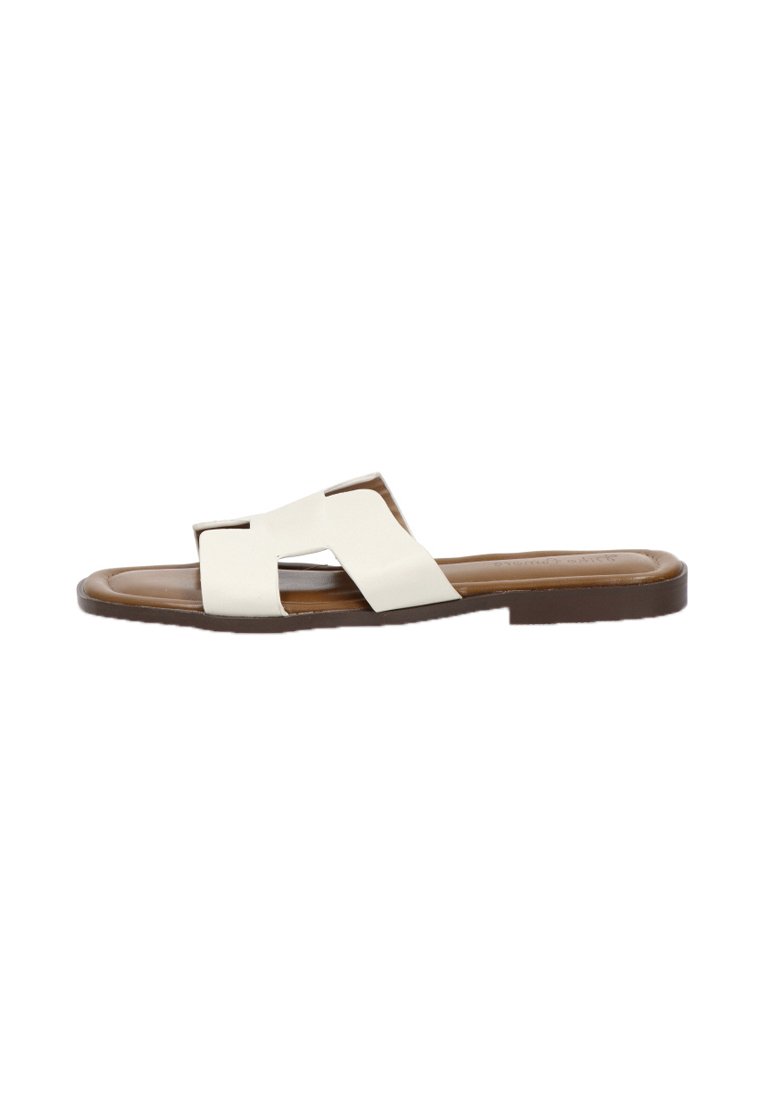 Sandalias planas de cuero blanco con dos correas cruzadas y una suela de goma marrón, que presentan una textura suave y un diseño minimalista.
