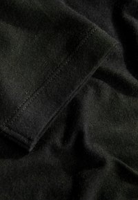 Tessuto nero con una texture liscia, caratterizzato da una manica piegata e cuciture ordinate lungo il bordo, che mostrano una finitura morbida.