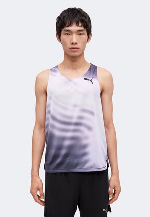 Jeune homme portant un maillot de sport sans manches Puma dégradé violet et un short noir Puma, debout devant un fond clair uni.
