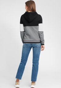 Huvtröja med svart, grå och vit färgblockdesign. Material av bomullsblandning, långa ärmar och känguruficka. Buren med blå jeans.