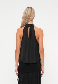 Top preto sem mangas com detalhe nas costas em forma de olho-chave, feito de tecido leve, apresentando um decote alto e um corte solto e fluido.