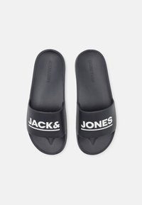 Fekete, textúrált felületű strandpapucs, amelyen fehér "JACK&JONES" logó található a pántokon. Lapos talp, sarok nélkül.
