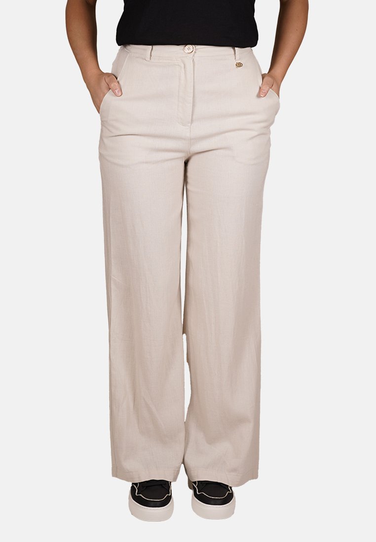 Pantaloni beige a gamba larga realizzati in tessuto leggero, con chiusura a bottone, tasche frontali e una texture liscia. Abbinati a scarpe nere.