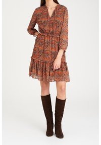 Kuosi mekko punaisen ja ruskean sävyissä, pitkähihaisena, V-pääntiellä, elastisella vyötäröllä ja kerroksellisella röyhelöhännällä. Yhdistetty ruskeisiin polvipitkiin saappaisiin.