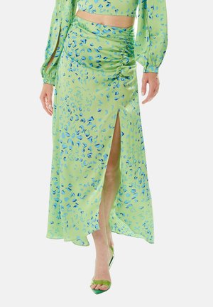 Green skirt with blue abstract print, featuring a high slit and ruching detail. Made of lightweight fabric, paired with matching green heels.