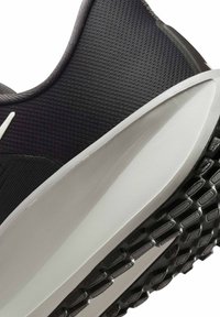 Primer plano de un tacón de zapatilla de correr negra y gris con suela texturizada y parte superior de tela de malla.