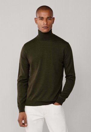 Suéter de cuello vuelto verde oscuro hecho de tejido de punto, con mangas largas y puños acanalados, combinado con pantalones blancos.