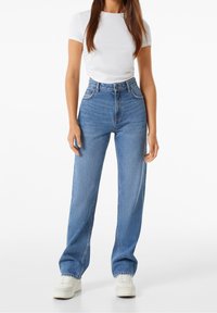 Jeans de mezclilla azul de cintura alta con un ajuste relajado, que cuentan con bolsillos frontales, cremallera y ligero desgaste a lo largo de las costuras.