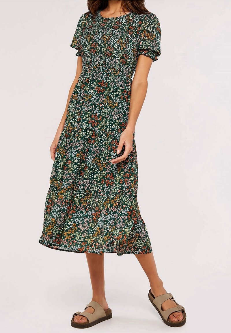 Robe verte à fleurs avec manches courtes bouffantes et ourlet à volants. Présente de petits motifs floraux colorés sur un fond sombre.