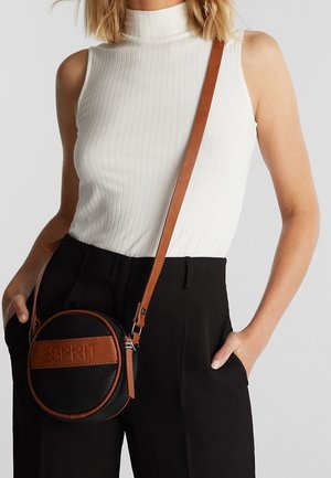 Schwarze, runde Tasche mit strukturierter Oberfläche, braunen Lederakzenten und einem Riemen. Verfügt über ein auffälliges Logo auf der Vorderseite.