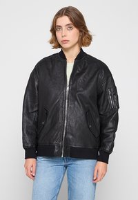 Svart läderbomberjacka med ribbat krage, frontdragkedja, sidofickor och en ficka med dragkedja på vänster arm. Slät textur.