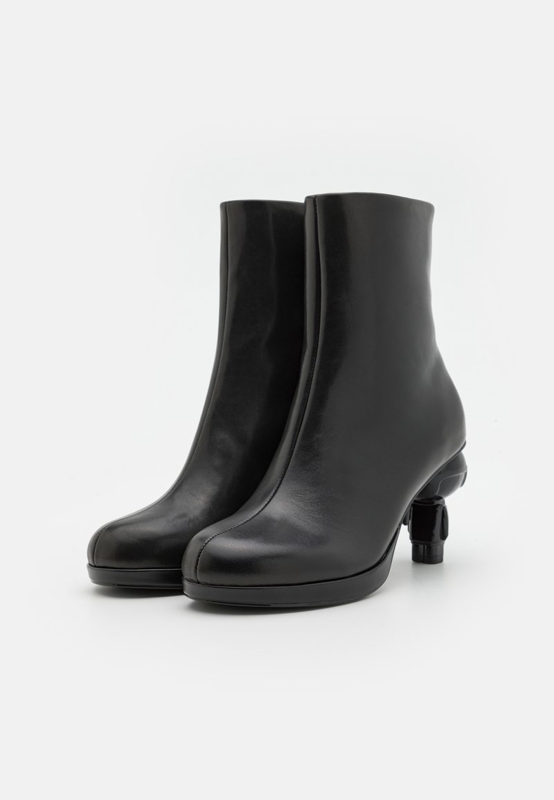 Schwarze Leder-Stiefeletten mit einem eleganten Design und abgerundetem Zehenbereich, ausgestattet mit einem einzigartigen Blockabsatz für Stabilität. Glatte Textur und minimalistischer Stil.