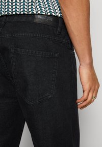 Jeans en denim noir au toucher lisse, dotés d'une poche arrière et d'une étiquette INDICODE au niveau de la taille.