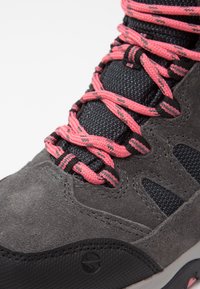 Gros plan d'une chaussure de randonnée en daim gris et mesh noir avec des lacets à motifs rose vif et noir passant à travers des œillets.