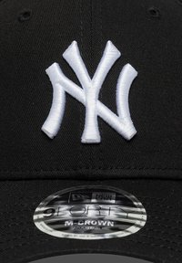 Boné de basebol preto com logótipo dos New York Yankees branco bordado em relevo. Apresenta uma copa arredondada e uma correia ajustável. Etiqueta da New Era visível.