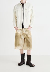 Ljus denimjacka, svart skjorta, bruna corduroy-shorts med randigt mönster, och bruna läderstövlar med spännvidd.