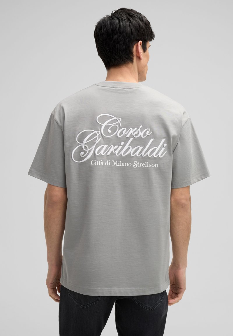 Grijze katoenen t-shirt met witte cursieve tekst op de achterkant: "Corso Garibaldi Città di Milano Strellson." Korte mouwen, relaxte pasvorm.