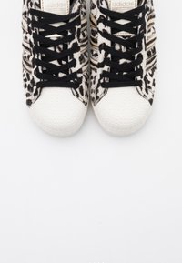 Czarno-białe trampki w leopardzi wzór z fakturowanym białym noskiem, czarnymi sznurowadłami i oznaczonym językiem. Płaska podeszwa.