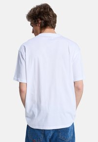 Hvid bomulds t-shirt med korte ærmer, ribbet halsudskæring og lige pasform, set fra ryggen.