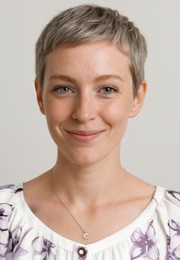 Biała bluzka z krótkim rękawem w purpurowy wzór kwiatowy, srebrny naszyjnik z zawieszką w kształcie półksiężyca, jasna skóra, krótkie szare włosy, neutralne tło.