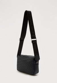 Mala de ombro preta com padrão em relevo, textura suave e alça ajustável com logótipo. Fecho com zíper e detalhe de hardware hexagonal.