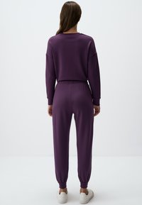 Paarse sweatshirt en joggingset van zachte stof, met een losse pasvorm, elastische tailleband en omgeslagen enkels. Witte sneakers.