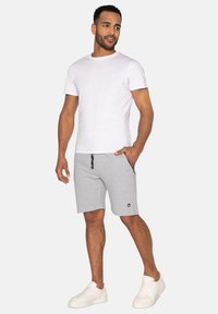 Hvid T-shirt og grå shorts med lommer, der har et diskret mærkelogo og snoreliv. Fodtøj: hvide sneakers.