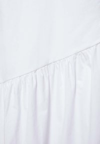Tissu blanc avec une couture diagonale et des plis froncés, révélant la texture et une apparence douce et légère.