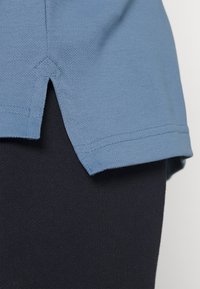 Ljusblå stickad skjorta med sidoredning, strukturväv och kontrasterande svart material undertill. Inga synliga mönster eller hårdvara.