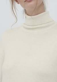 Maglione a collo alto color crema realizzato in morbido tessuto a maglia. Presenta un collo a coste e una superficie liscia con minimi dettagli.