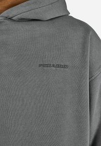 Felpa con cappuccio grigia con logo "PEGADOR" in rilievo sul lato sinistro del petto, che mostra la trama del tessuto e i dettagli della cucitura della spalla.