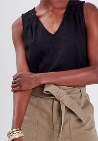 Haut noir sans manches avec col en V et détails en dentelle sur l'épaule. Porté avec un pantalon taille haute beige clair ceinturé à nouer.