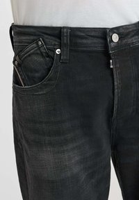 Jean noir en denim avec une coupe droite, comportant une poche avant, un bouton en métal, et des détails de couture subtils. Le matériau semble doux et texturé.