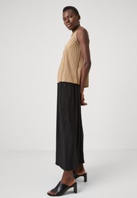 Beige, plissert topp uten ermer kombinert med en svart plissert maxiskjørt og svarte blokkhæl mules. Glatt tekstur, flytende design.