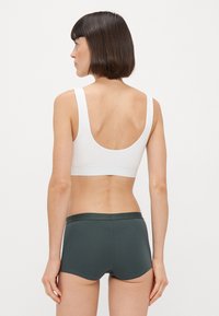 Sutiã desportivo branco com costas baixas, combinado com calções hipster verdes escuros com um cós elástico. Design simples e sem costuras.