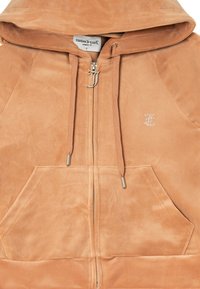 Felpa con zip di colore marrone chiaro in morbido suede, dotata di cappuccio, tasche frontali e un logo decorativo in cristalli sul petto a sinistra.