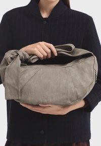 Šedá kožená taška přes rameno s uzlovou rukojetí, s hladkým povrchem, ostrým designem a jemným logem na přední straně.