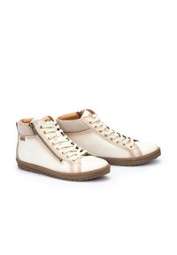 Zapatillas altas de cuero crema con ojales dorados, detalle de cremallera, acentos beige y una suela de goma marrón texturizada.