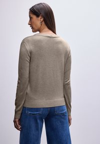 Maglione beige con collo rotondo, polsini e orlo a costine. Indossato con jeans a gamba larga blu, che mostrano una texture in maglia e un design informale.