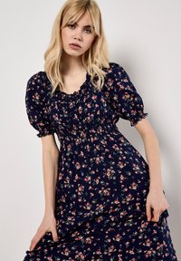 Marineblaues Blumen Kleid mit puffärmel, gerafftem Ausschnitt und gestreiftem Taillenbereich. Es hat kleine rosa und grüne Blumenmuster überall.