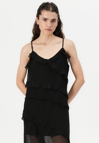 Robe noire en tissu léger, ornée de volants superposés au niveau de l'ourlet, de fines bretelles et d'une coupe fluide et ample.