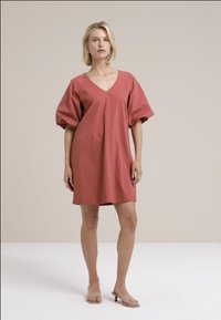Rochie cu mânecă scurtă, până la genunchi, de culoare roz prăfuit, cu decolteu în V, croială lejeră și țesătură din bumbac moale cu o textură netedă.
