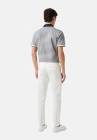 Heren polo met korte mouwen en een marineblauwe kraag, grijs en witte strepen, gecombineerd met slim-fit witte broek en witte sneakers.
